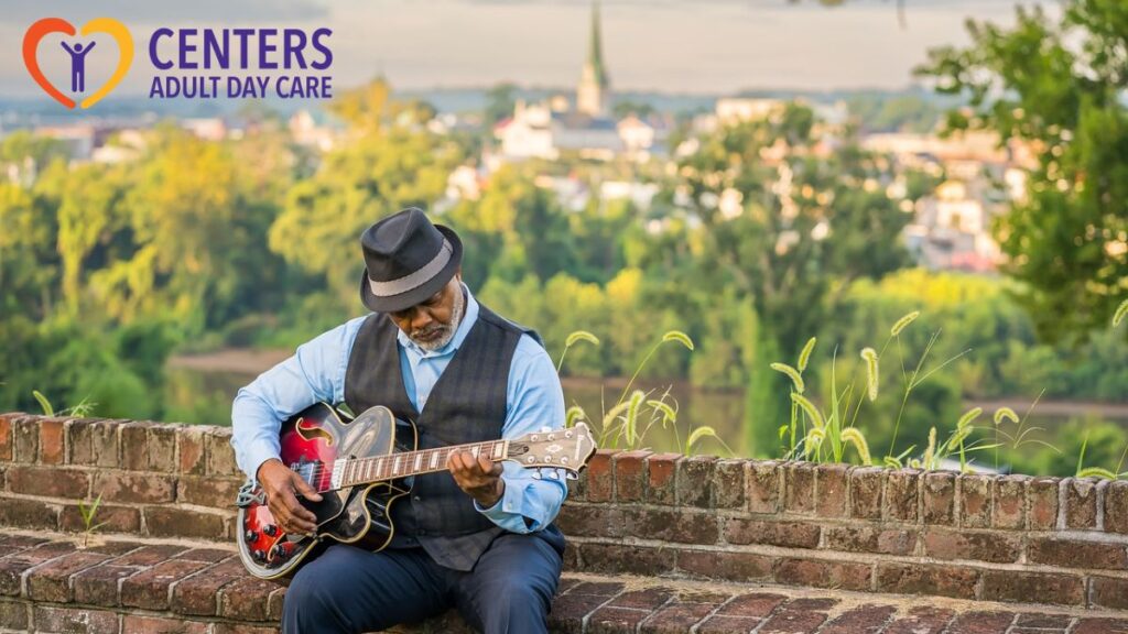 An elderly man plays the guitar enthusiastically outdoors, surrounded by greenery.
