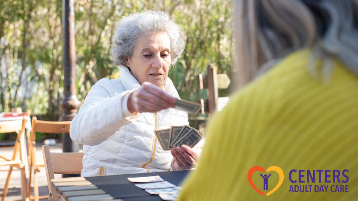 Adult day care in Richmond, a senior woman plays cards at a table with trees in the background.