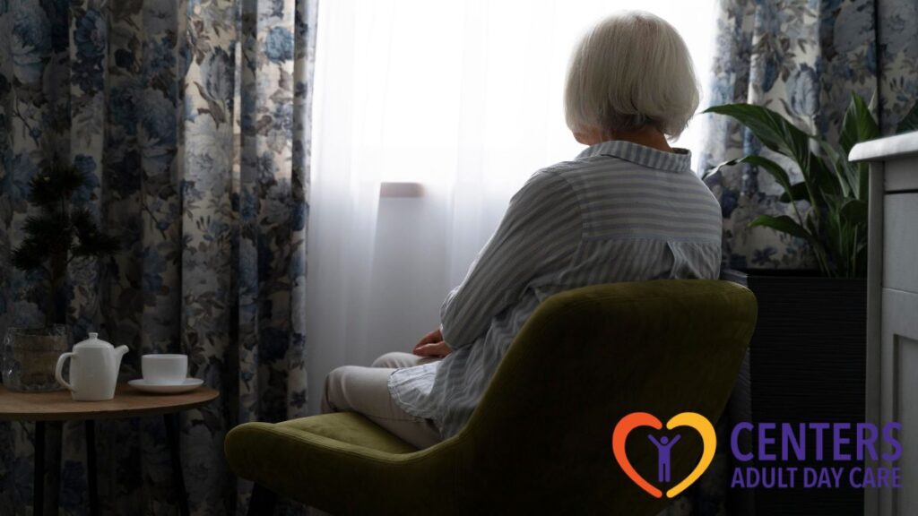 A senior woman gazes thoughtfully out a window at dusk, dappled light filling the room, illustrating calm and reflective moments in adult day care for your parent.