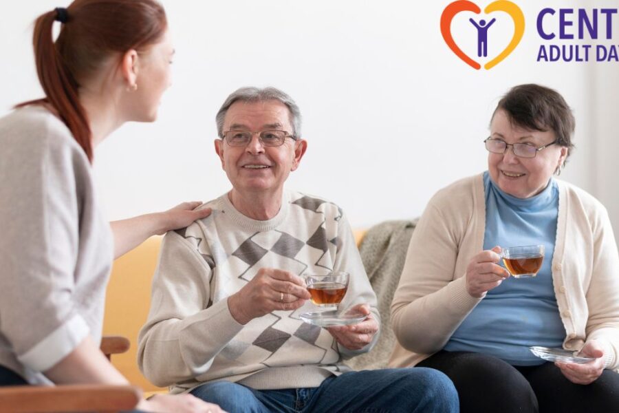 Senior couple sitting on a sofa, looking up at a caregiver while having an engaging conversation about care options.