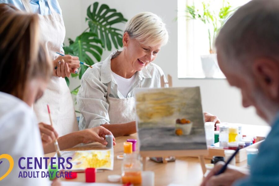 A group of seniors wearing aprons works on a crafting activity, with one senior woman in focus at a table filled with paint and art supplies.