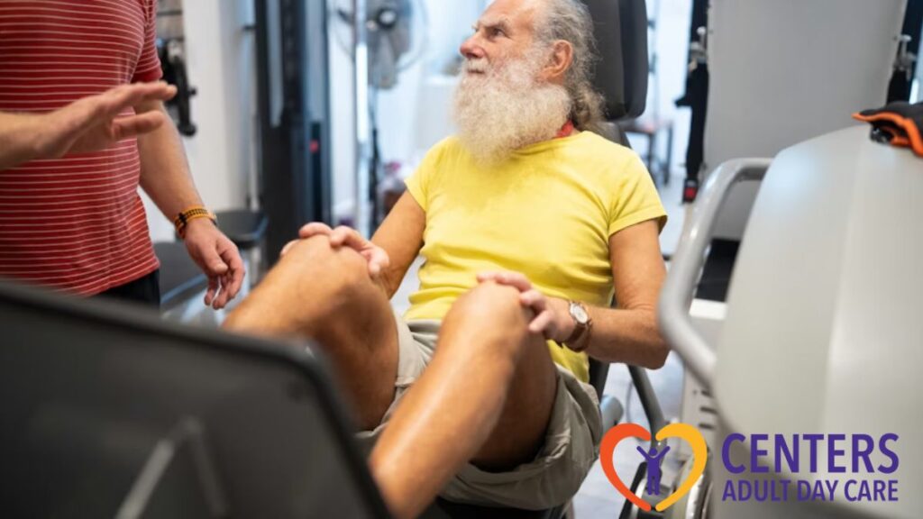 A senior man smiles at his therapist while pressing a leg plate exercise machine during physical therapy.